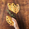 Wooden leaf-shaped cutting boards on a wooden surface with a hand holding one board.
