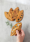 Three wooden leaf-shaped cutting boards with holes on a gray surface.