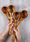 Four wooden spoons held by hands against a gray background
