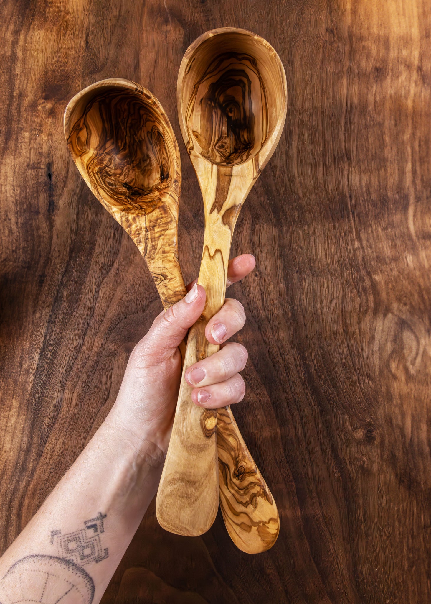 Two wooden spoons held by a hand against a wooden background
